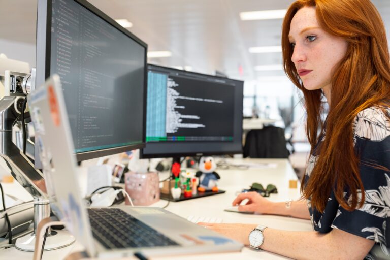 A woman working on multiple monitors in her office. Photo by thisisengineering on Unsplash.